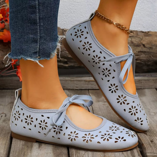 Blue perforated shoes with lace-up design worn by a person on a stone surface.