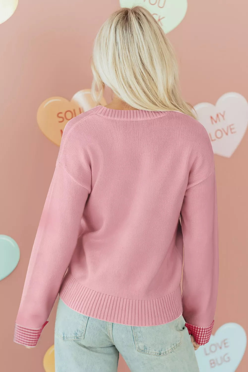 Person wearing a pink sweater with a heart-themed background