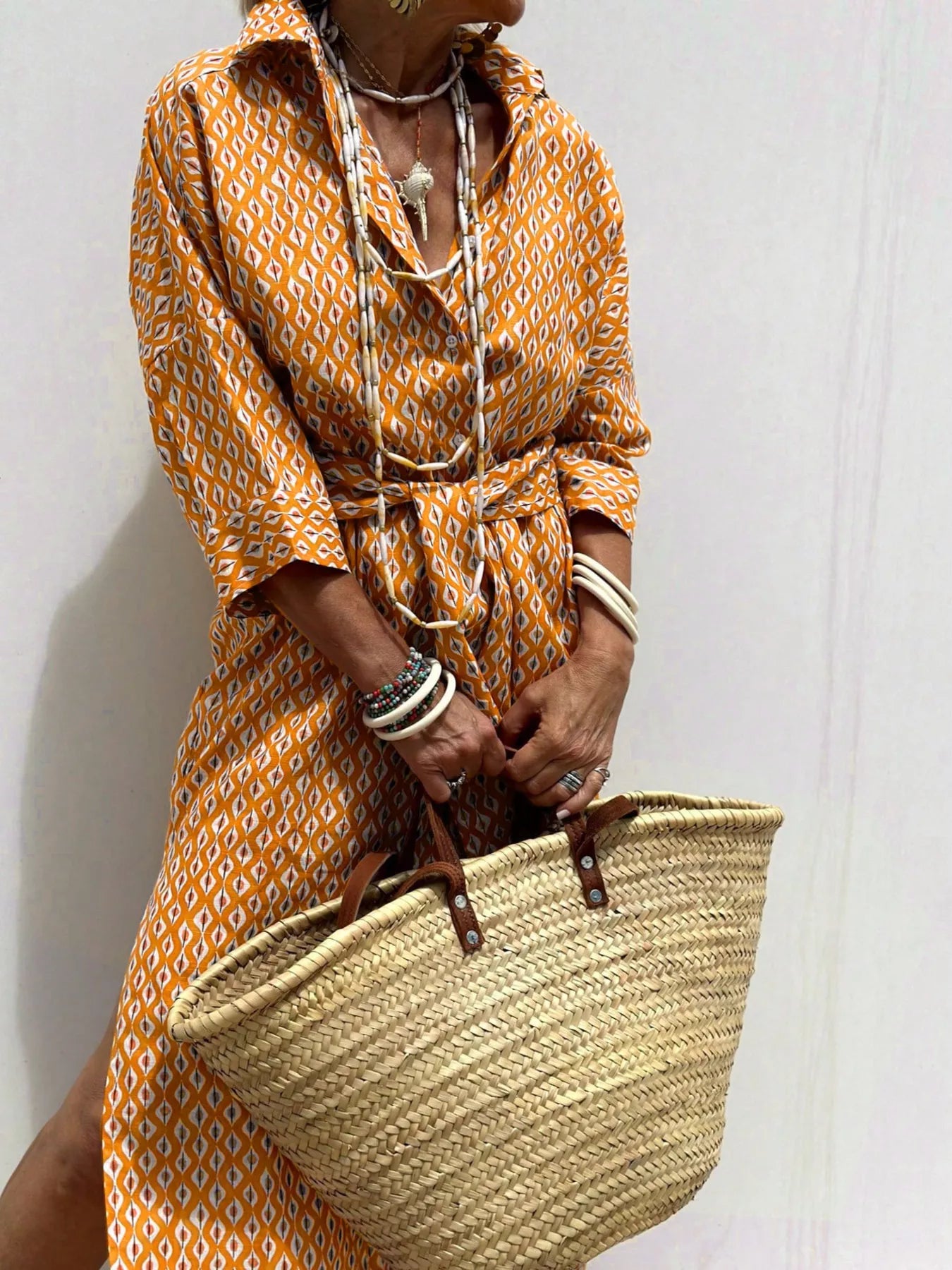 Person wearing a patterned dress holding a straw bag against a white background