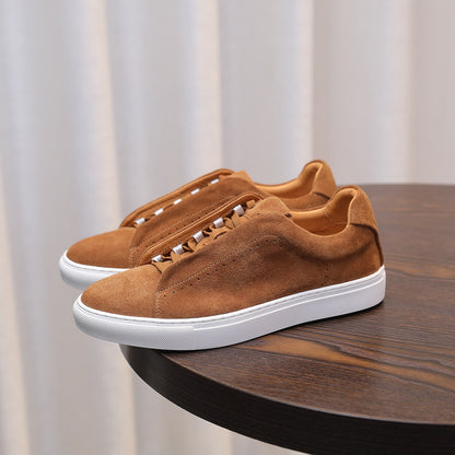 Pair of brown suede sneakers with white soles on a wooden surface.