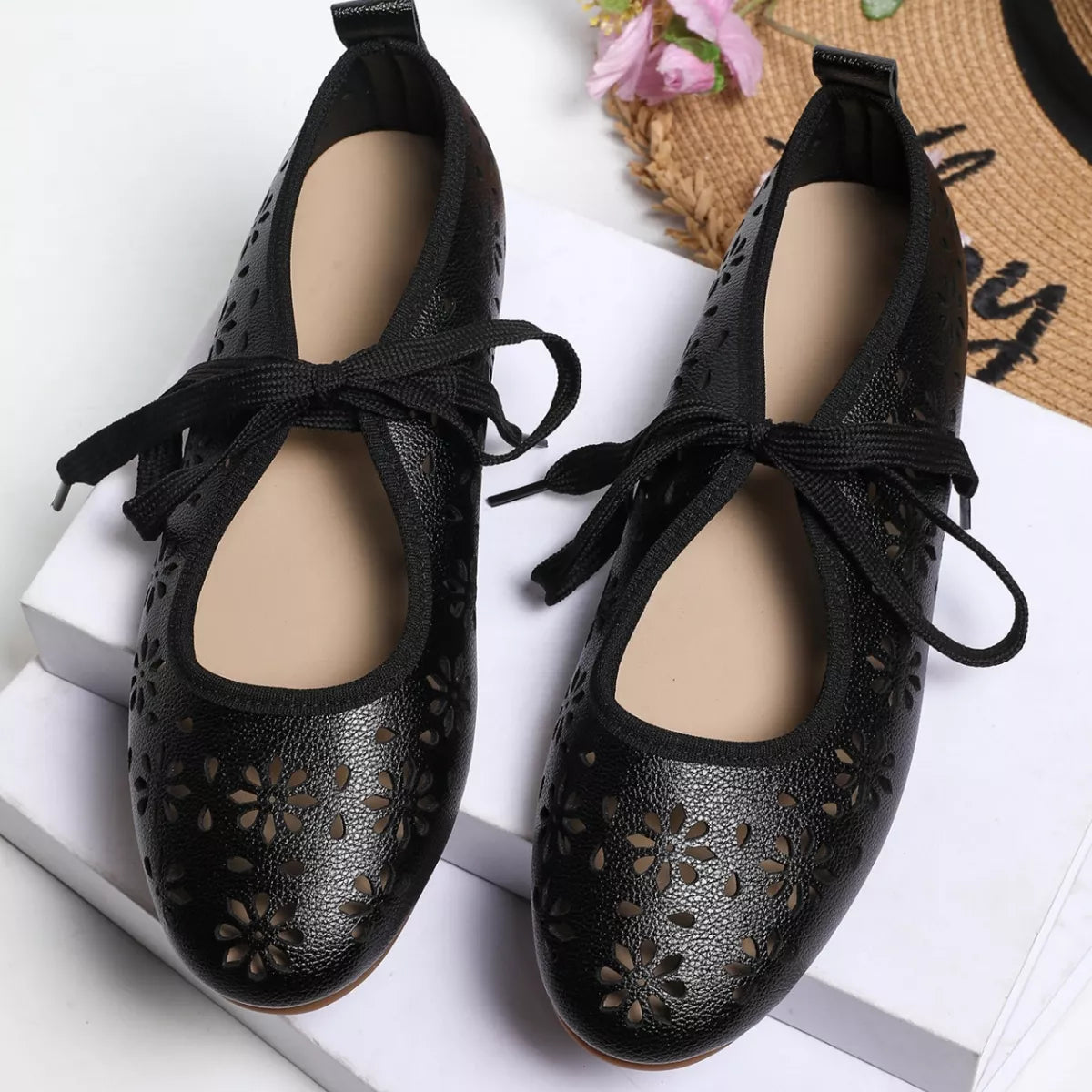 Black perforated flats worn with blue jeans on a neutral background