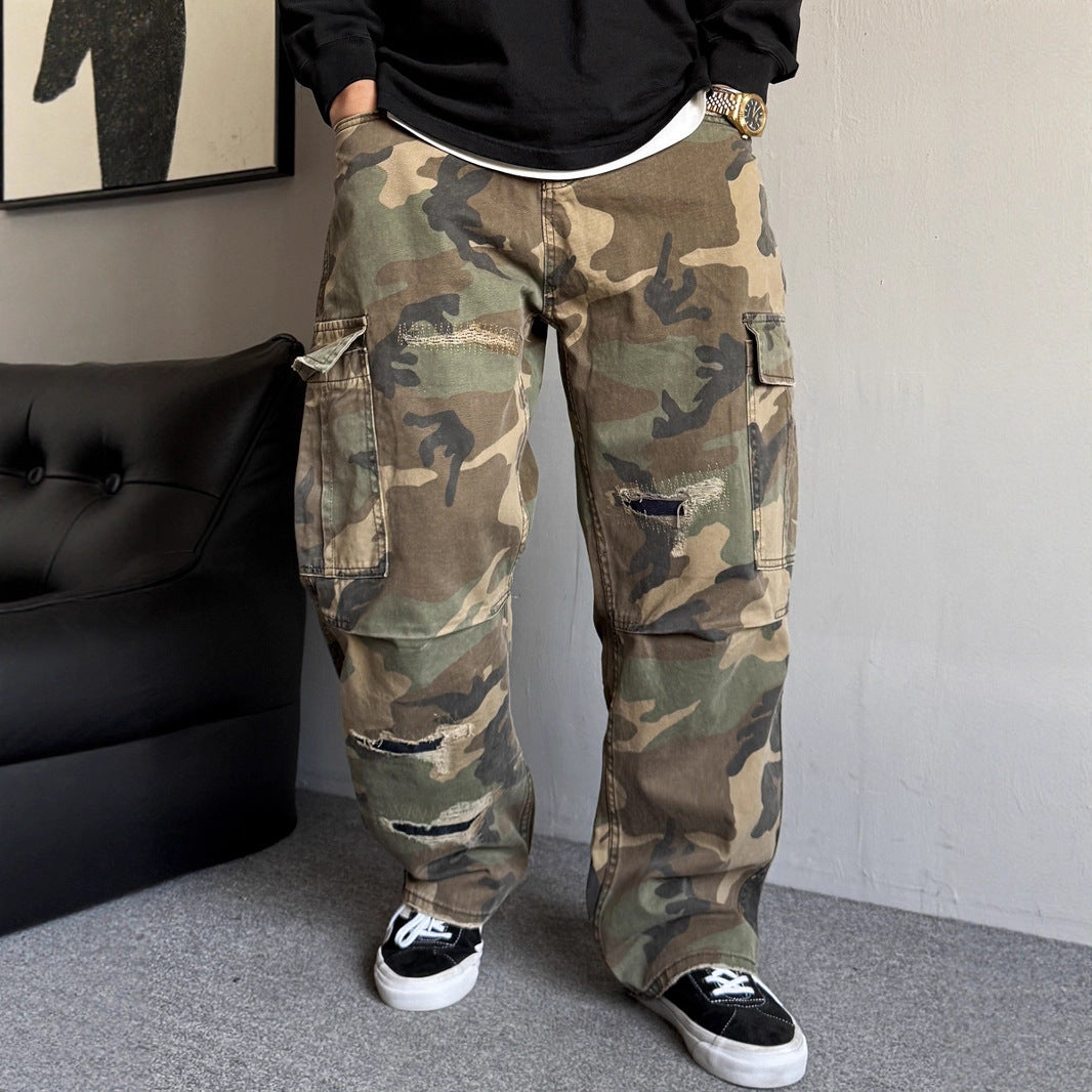 Person wearing camouflage pants in a room with a black couch and framed picture.
