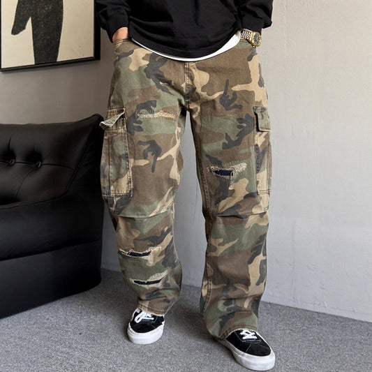 Person wearing camouflage pants in a room with a black couch and framed picture.
