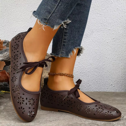 Brown perforated shoes with lace-up design worn by a person on a stone surface.