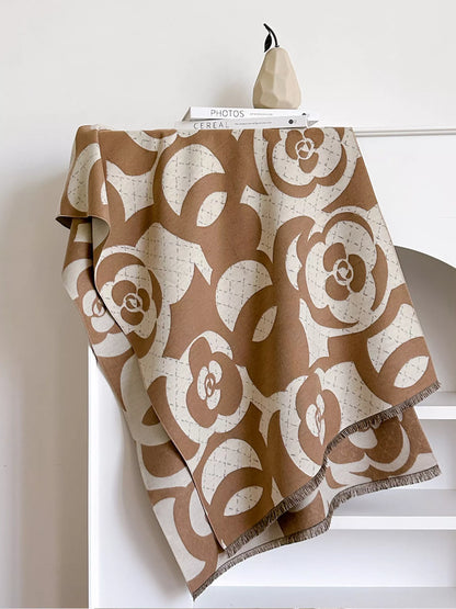 Brown and beige patterned throw blanket draped over a chair against a white wall.