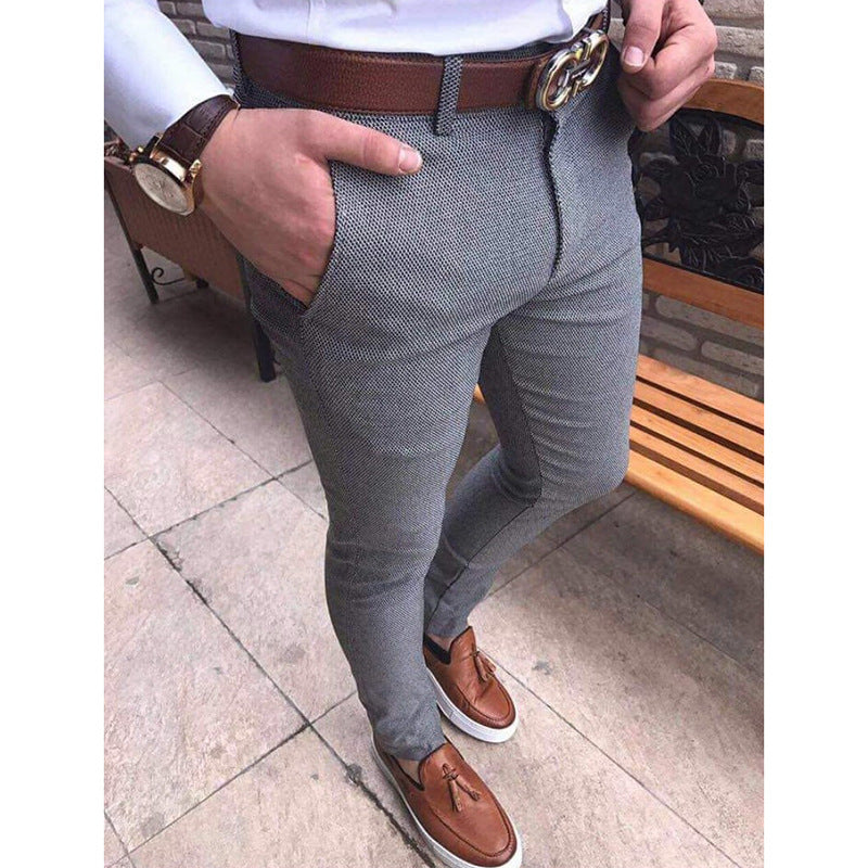 Person wearing gray pants with a brown belt and shoes, standing on a stone pavement.
