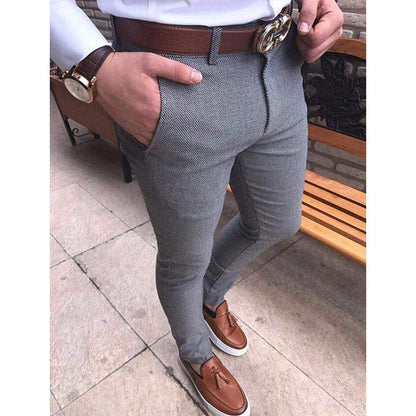 Person wearing gray pants with a brown belt and shoes, standing on a stone pavement.