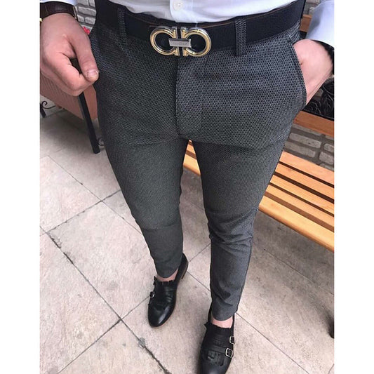 Person wearing dark gray patterned pants with a gold belt buckle on a tiled floor.