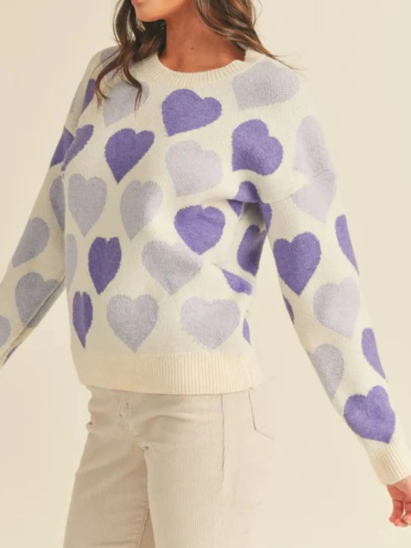 Sweater with purple and gray heart pattern worn by a person on a beige background
