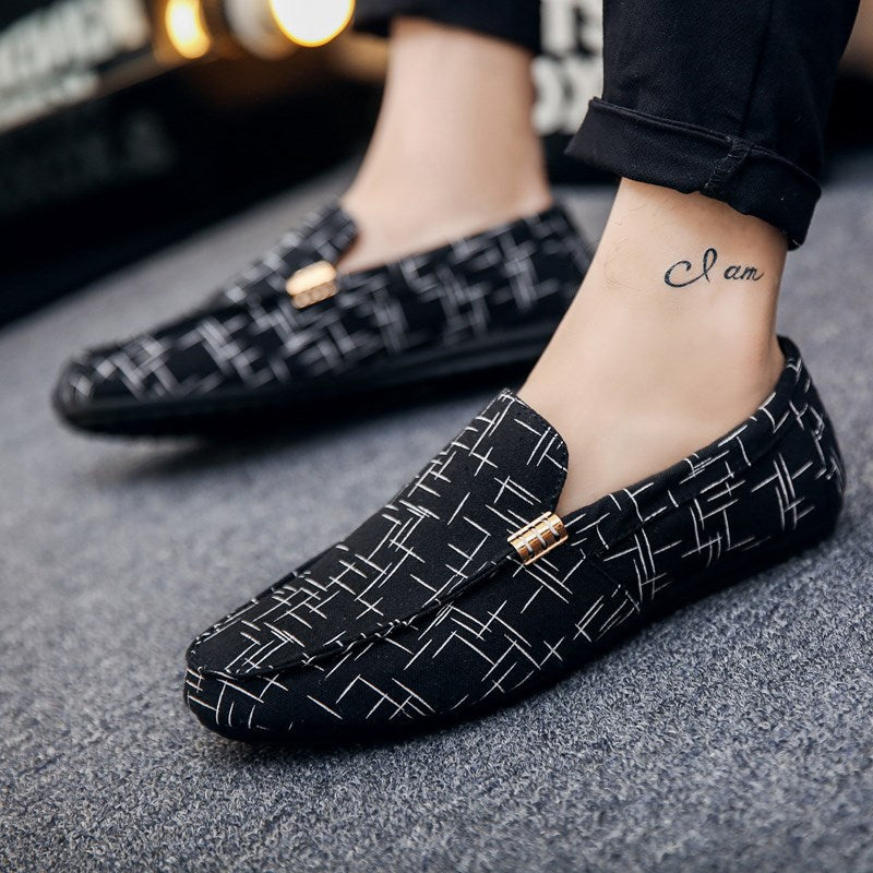 Black loafers with white geometric pattern worn by a person on a gray floor.