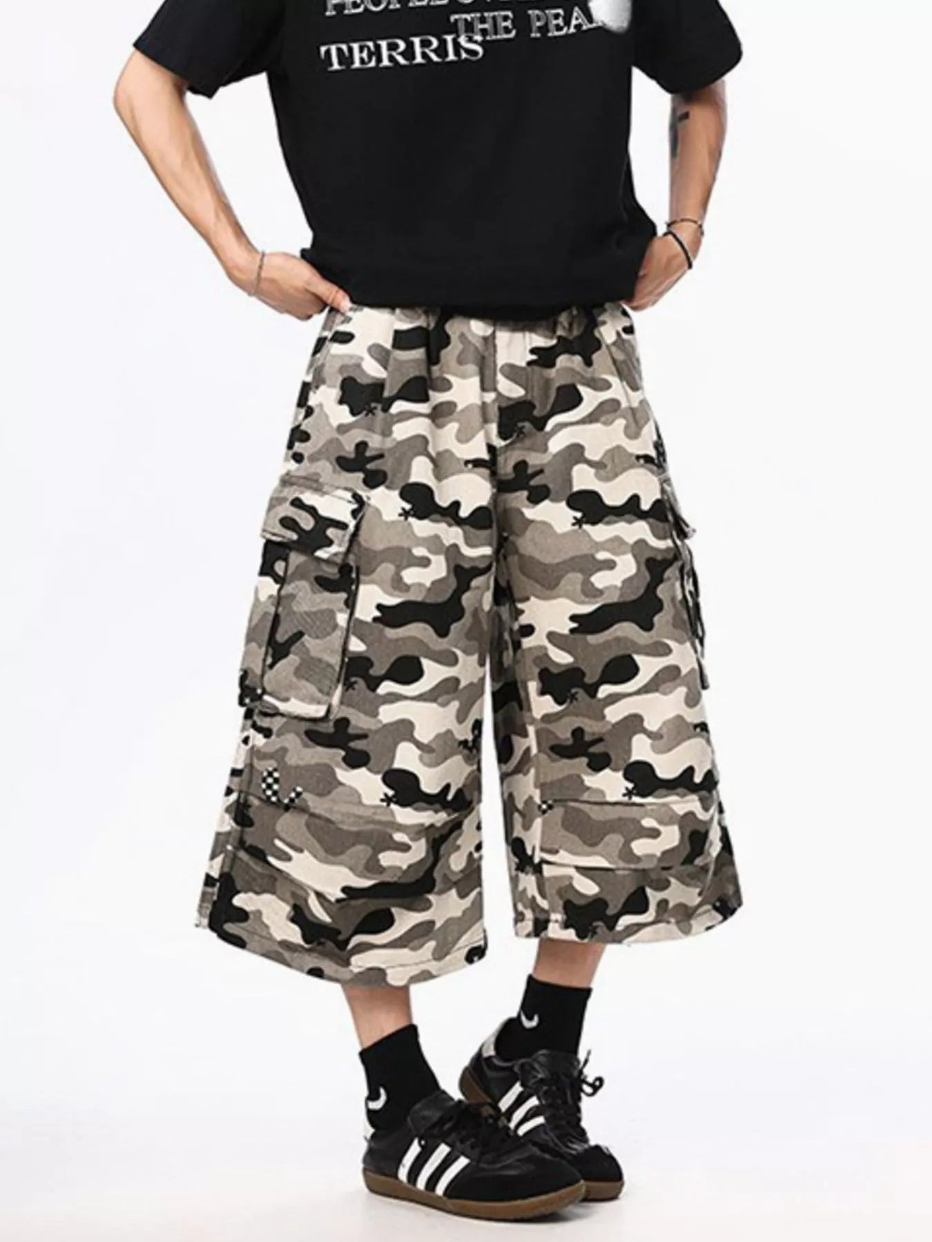Person wearing a black t-shirt with text and camouflage wide-leg pants on a white background