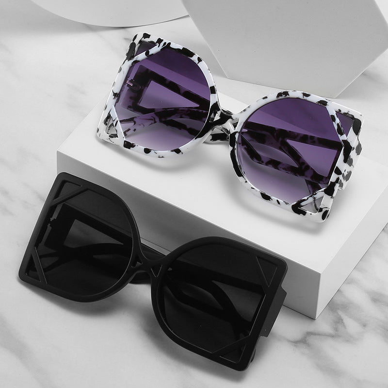 Two pairs of sunglasses, one with a leopard print frame and purple lenses, the other with a black frame, on a white surface.