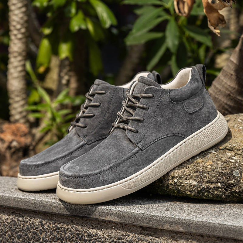 Gray suede shoes with white soles on a stone surface with green foliage in the background