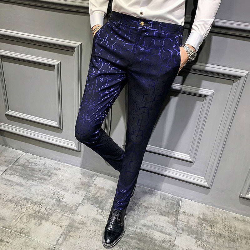 Person wearing a white shirt and blue patterned pants against a gray paneled wall.
