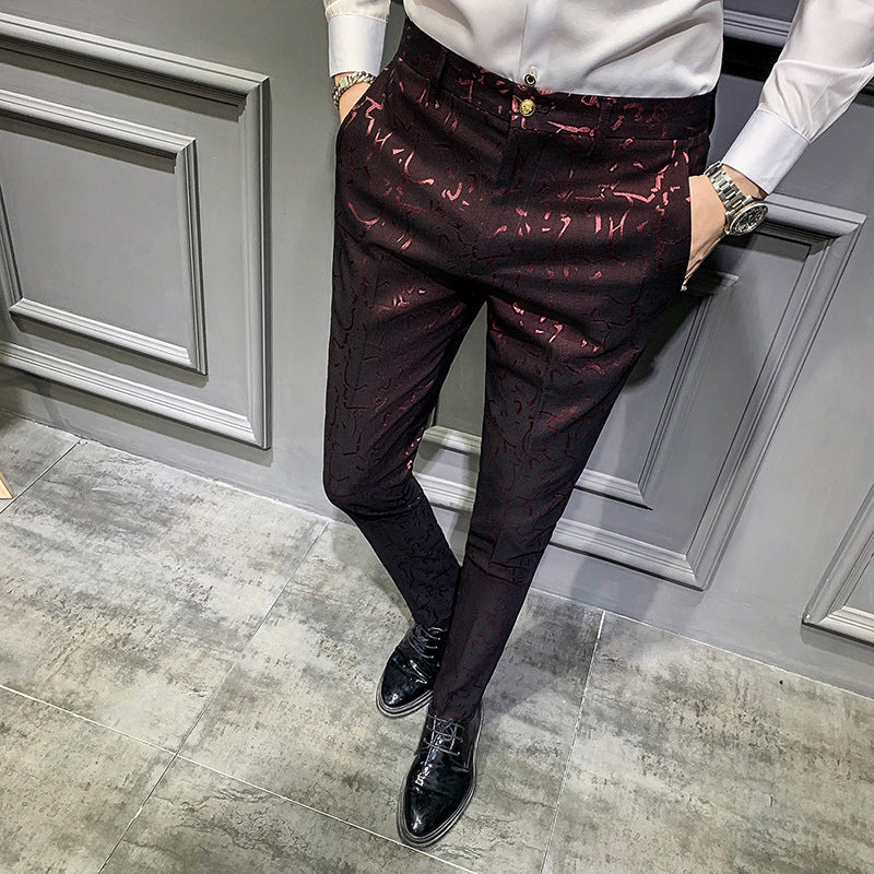 Person wearing a white shirt and red patterned pants standing against a gray wall.