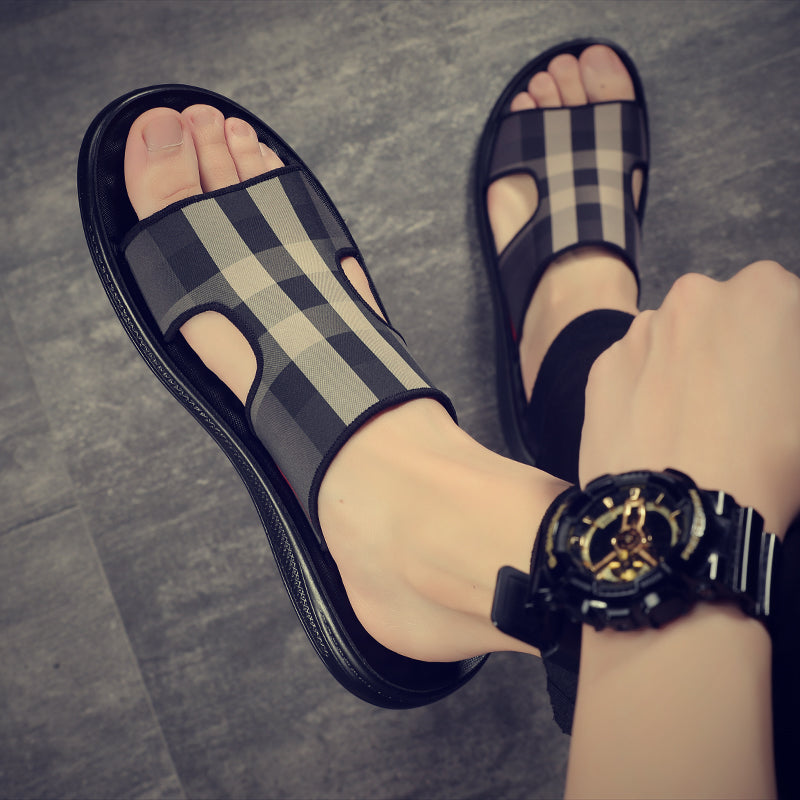 Black and gray checkered sandals worn on feet with a watch on wrist, on a gray floor.