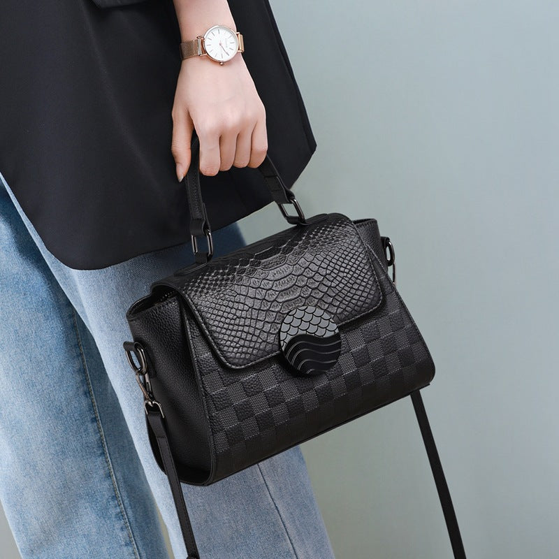 Black textured handbag held by a person wearing a black top and blue jeans against a light gray background