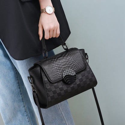 Black textured handbag held by a person wearing a black top and blue jeans against a light gray background