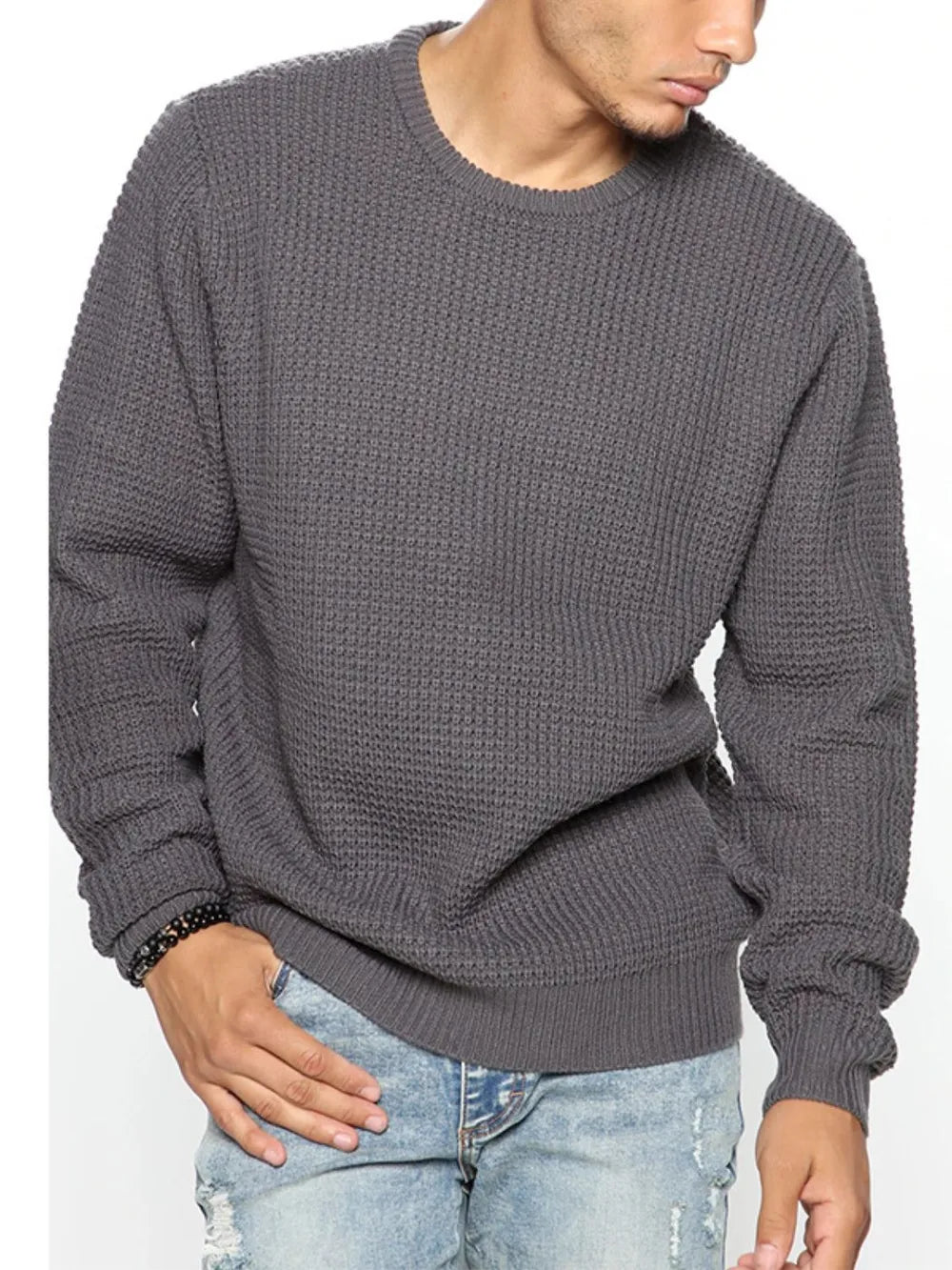 Person wearing a gray knitted sweater and light blue jeans on a white background