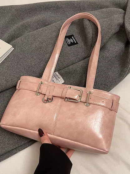 Pink handbag with a silver buckle held by a hand on a gray fabric background