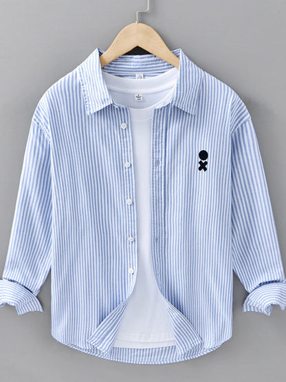 Blue and white striped shirt with a small black design on a hanger against a gray background