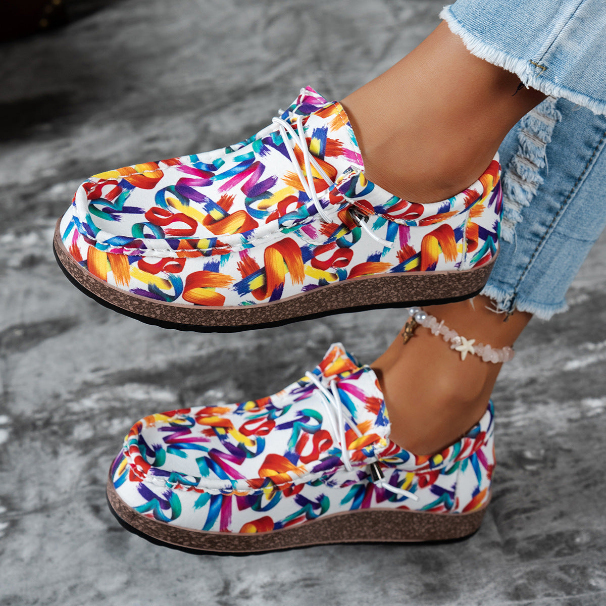 Colorful patterned shoes worn with denim jeans on a gray surface