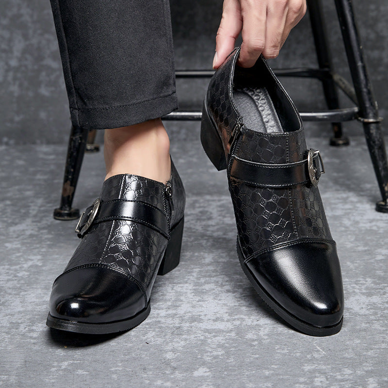 Black leather shoes with buckle details on a gray floor.
