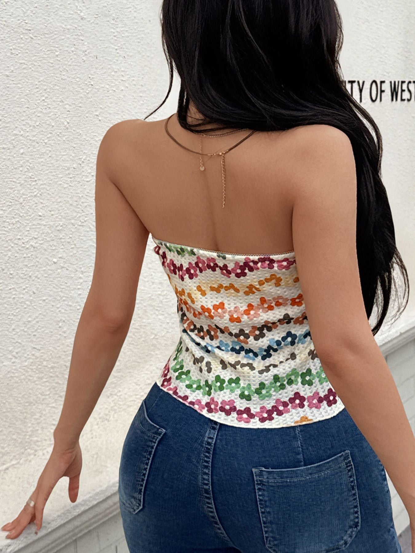 Woman wearing a colorful striped top and blue jeans against a white wall.