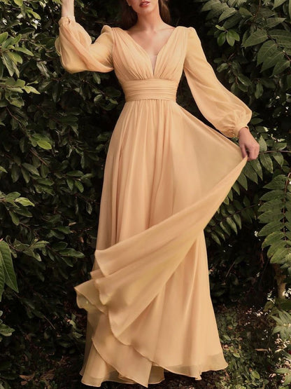 Woman wearing a long, flowing beige dress against a green leafy background