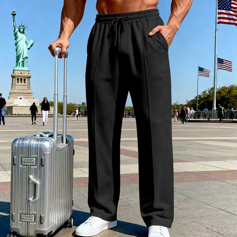Person wearing black pants standing next to a silver suitcase with the Statue of Liberty and American flags in the background.