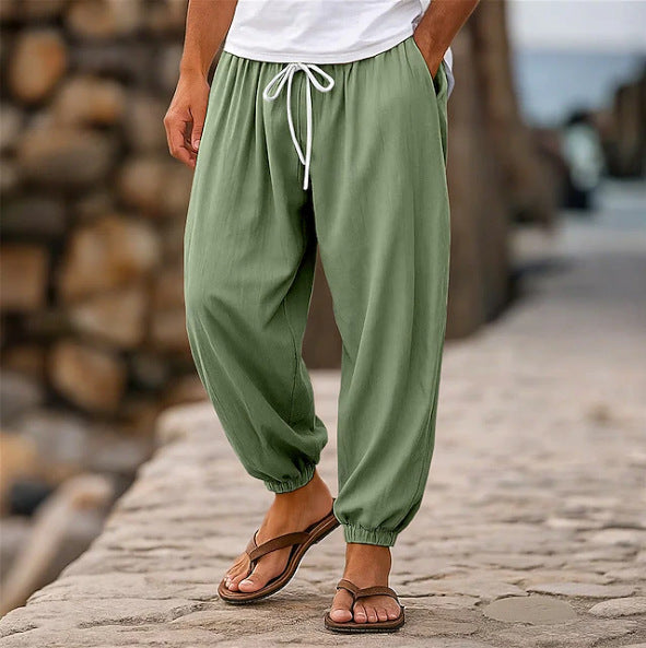 Person wearing green baggy pants and brown sandals standing on a stone path with a wooden log pile in the background.
