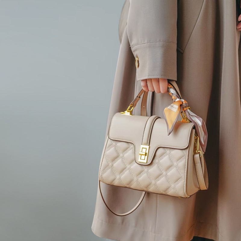 Beige quilted handbag with gold accents held by a person wearing a beige coat against a neutral background