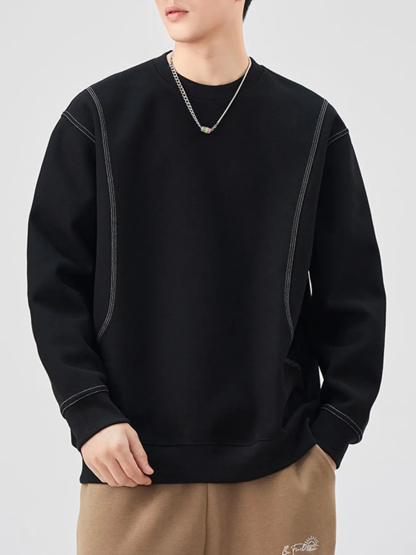 Person wearing a black sweatshirt with white stitching on a light gray background