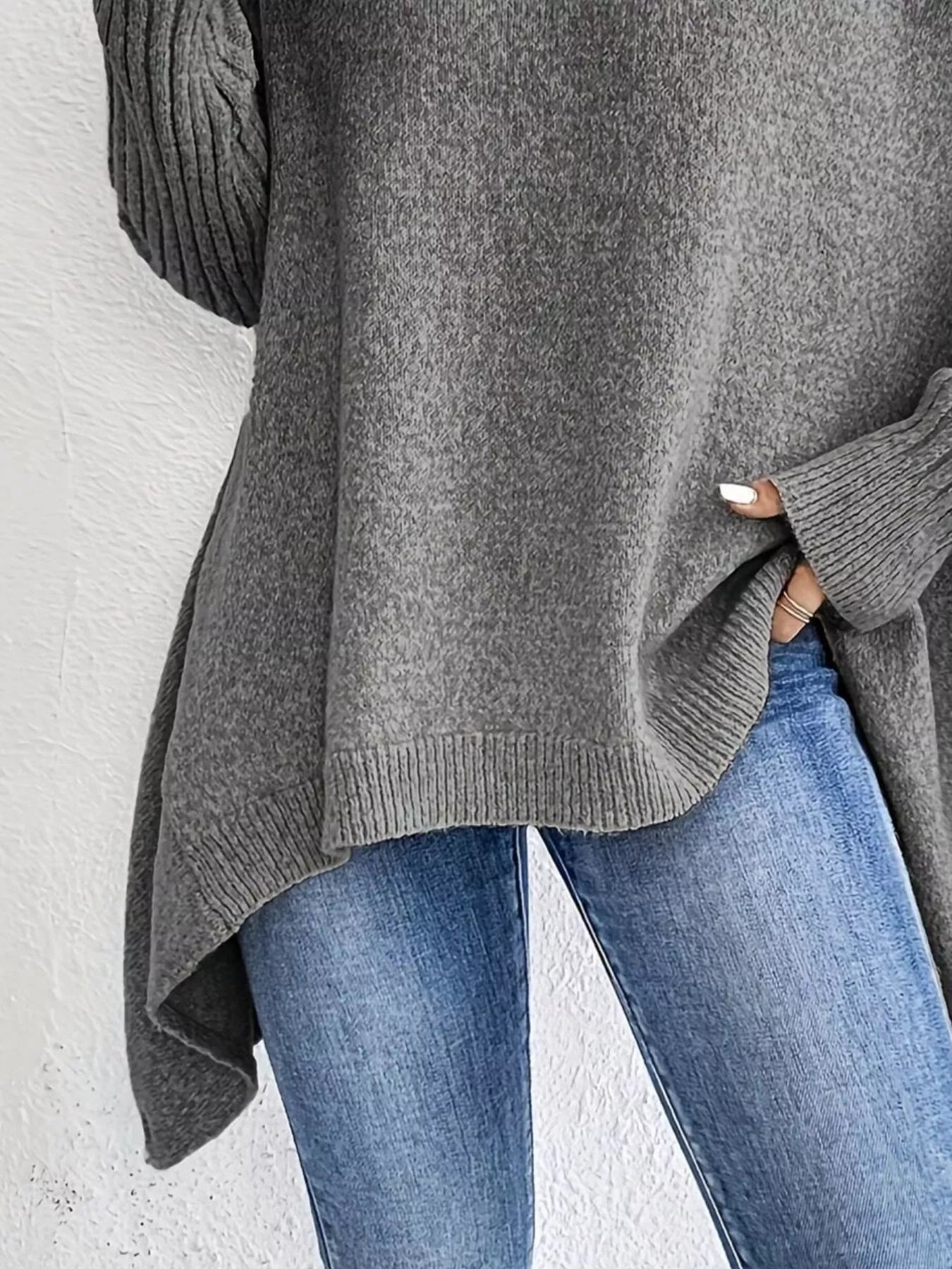 Person wearing a gray sweater and blue jeans against a white background