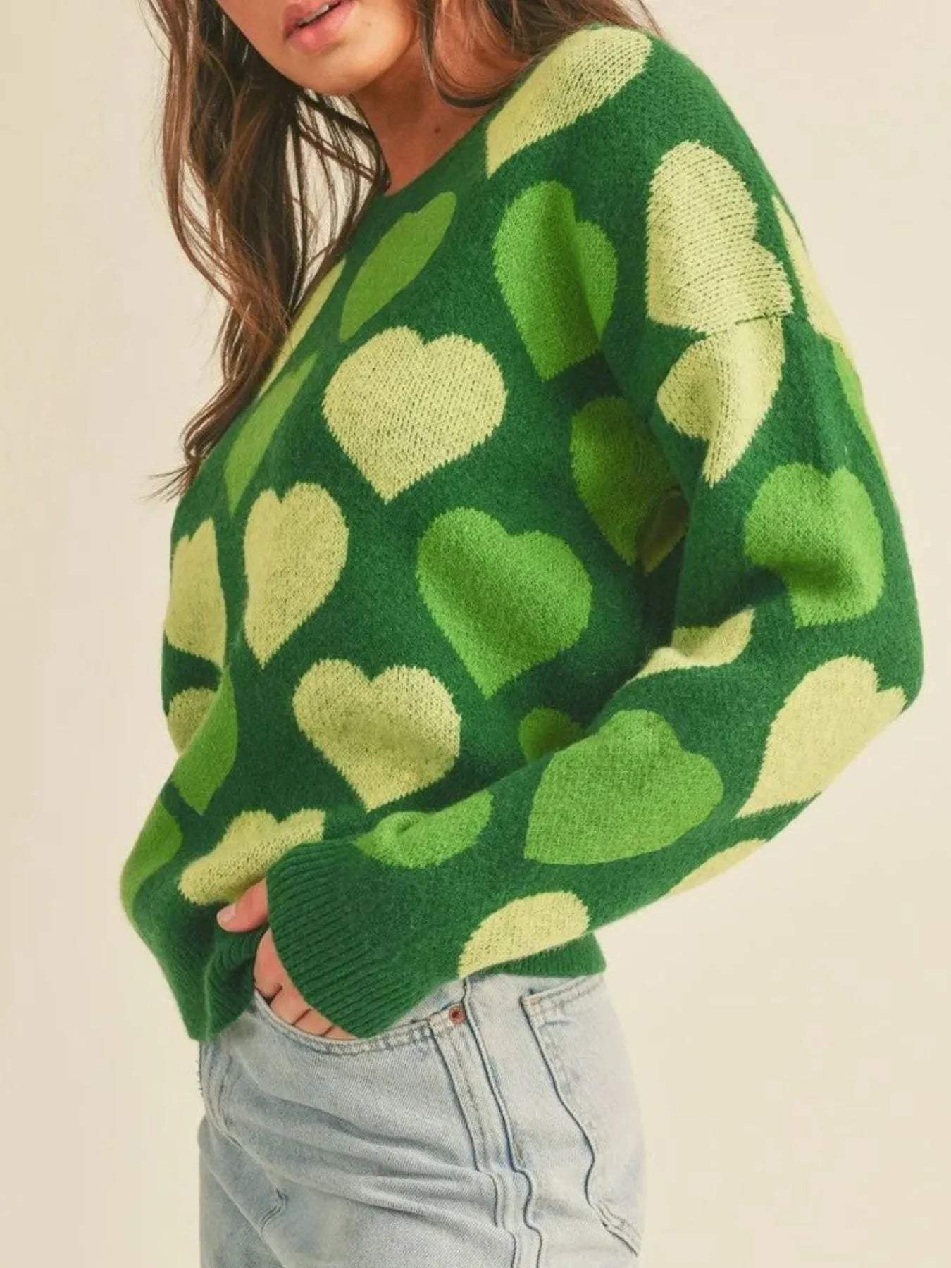 Person wearing a green sweater with heart patterns on a beige background