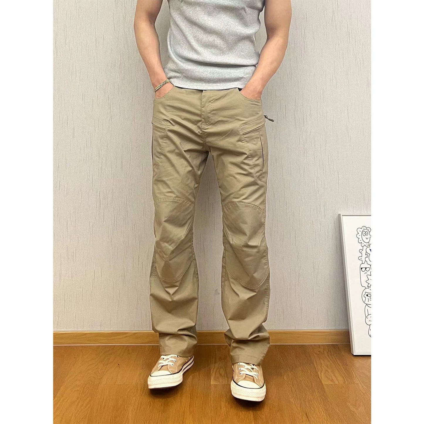 Person wearing beige pants and a gray shirt against a plain wall.