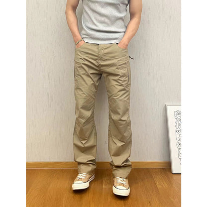 Person wearing beige pants and a gray shirt against a plain wall.