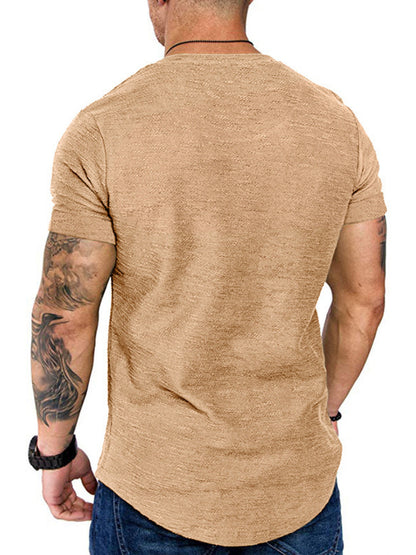 Man wearing a beige t-shirt with tattoos visible on arms, on a white background