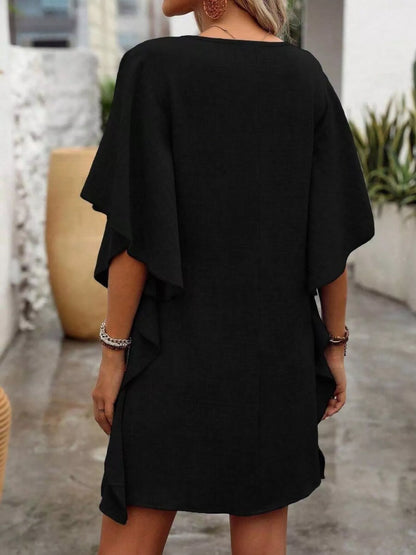Person wearing a black dress with ruffled sleeves in an outdoor setting.
