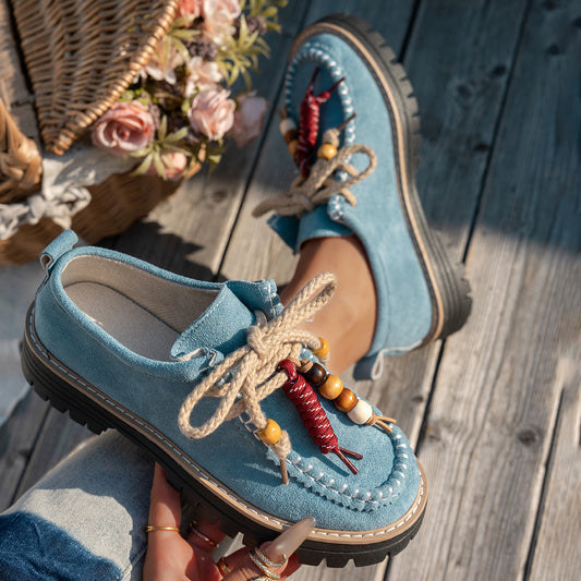 Blue loafers with decorative laces held by a person on a wooden surface.