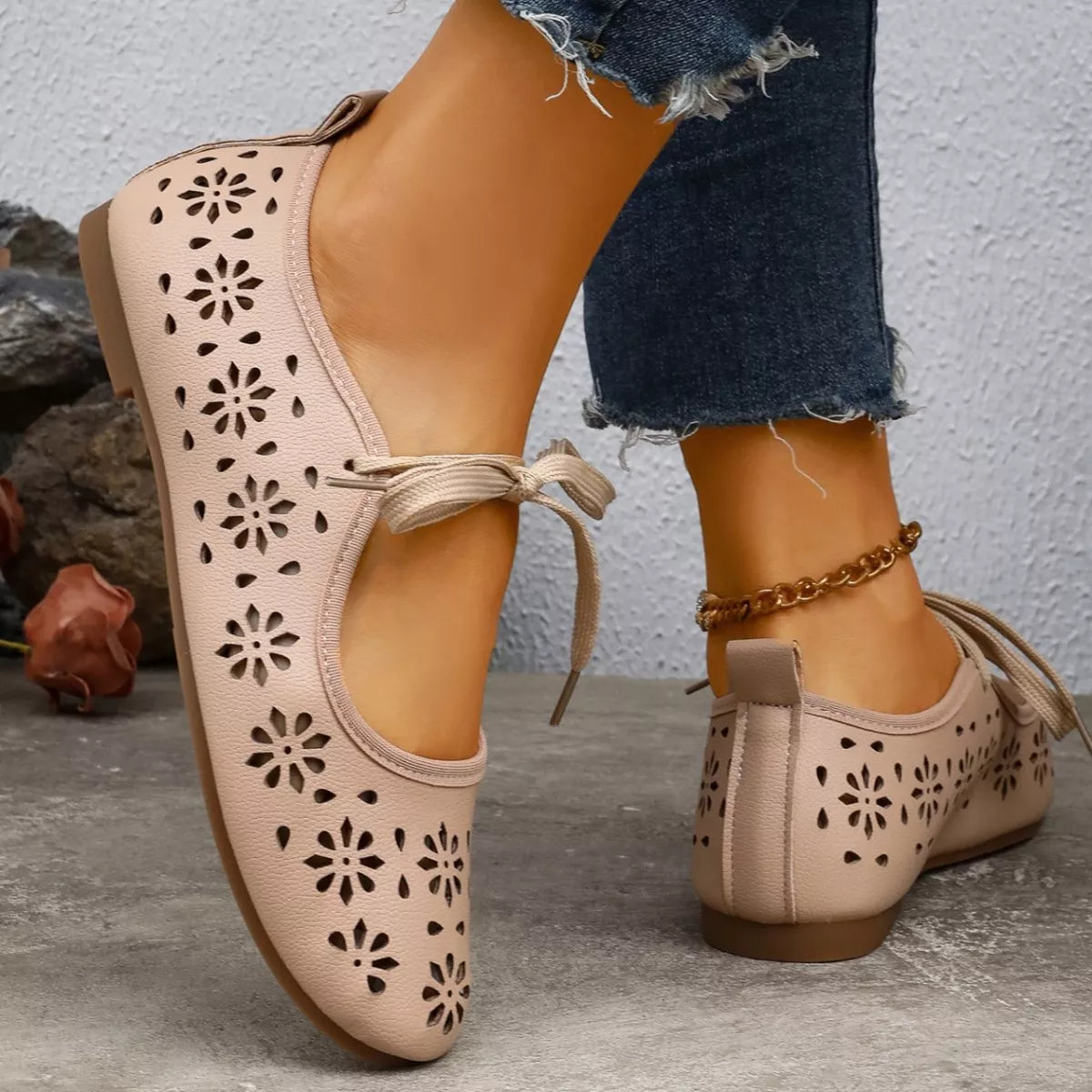 Pair of pink ballet flats with floral cutouts on a stone surface