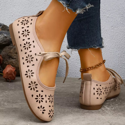 Pair of pink ballet flats with floral cutouts on a stone surface