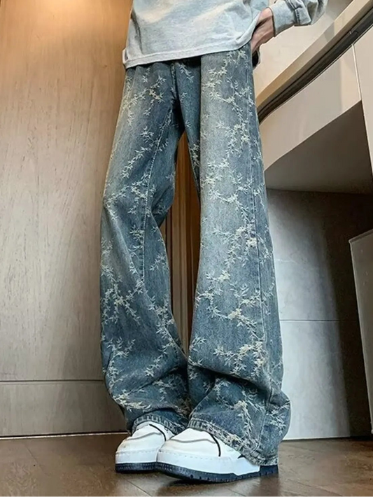 Person wearing a light gray sweatshirt with text and distressed blue jeans indoors.