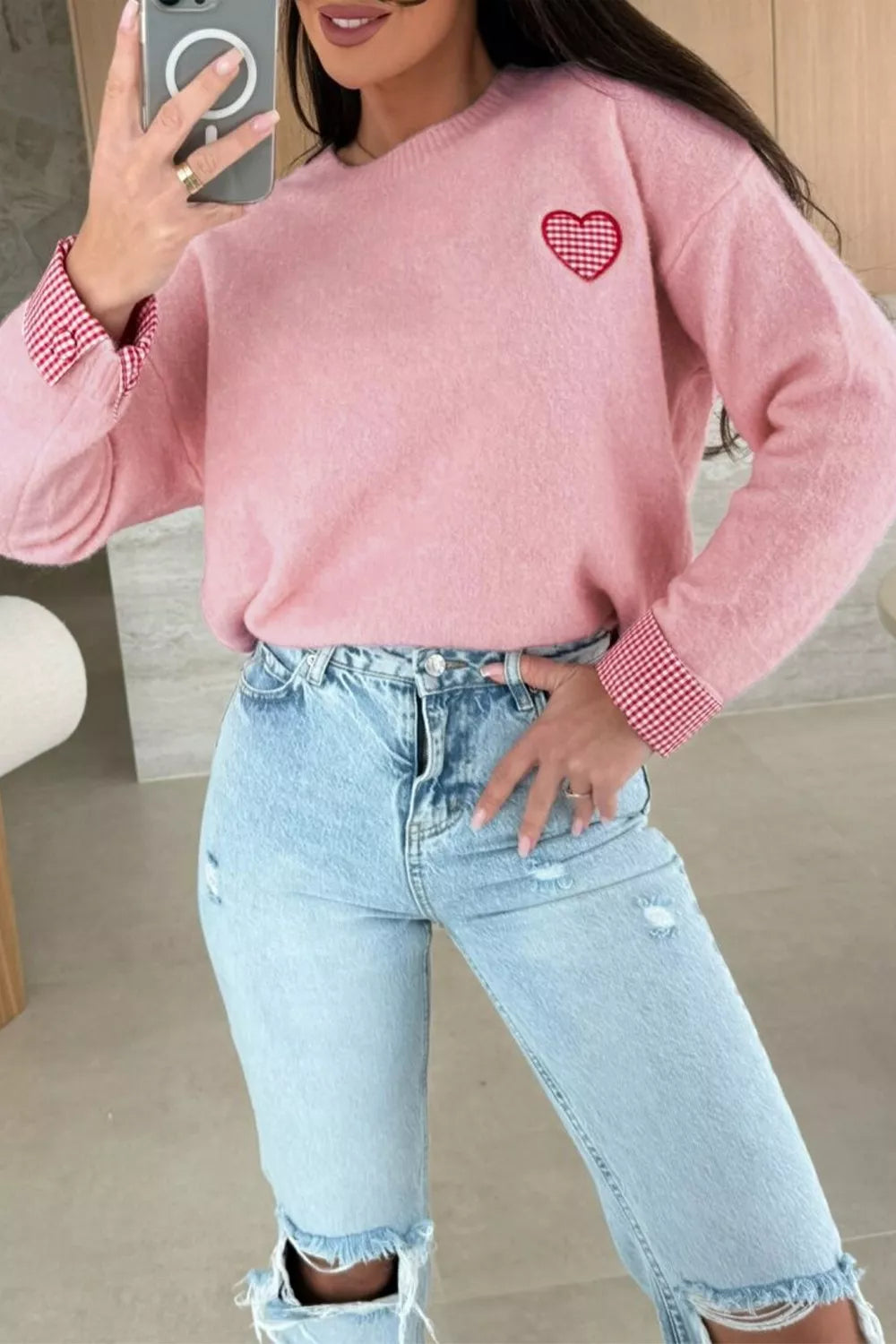 Person wearing a pink sweater with a heart design and light blue jeans indoors.