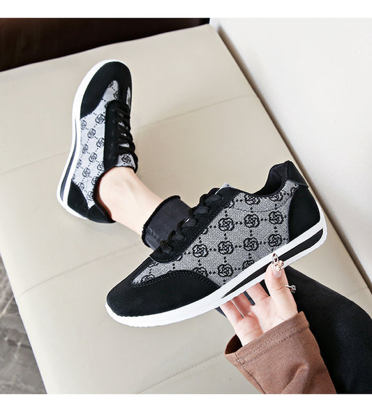 Black and gray patterned sneakers being held up on a light-colored surface.
