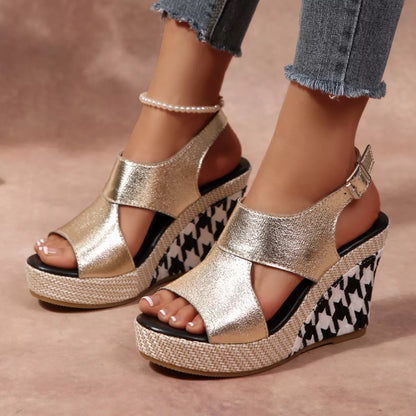 Gold wedge sandals with houndstooth pattern worn by a person, with a blurred floral 