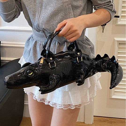 Person holding a black alligator-shaped handbag indoors