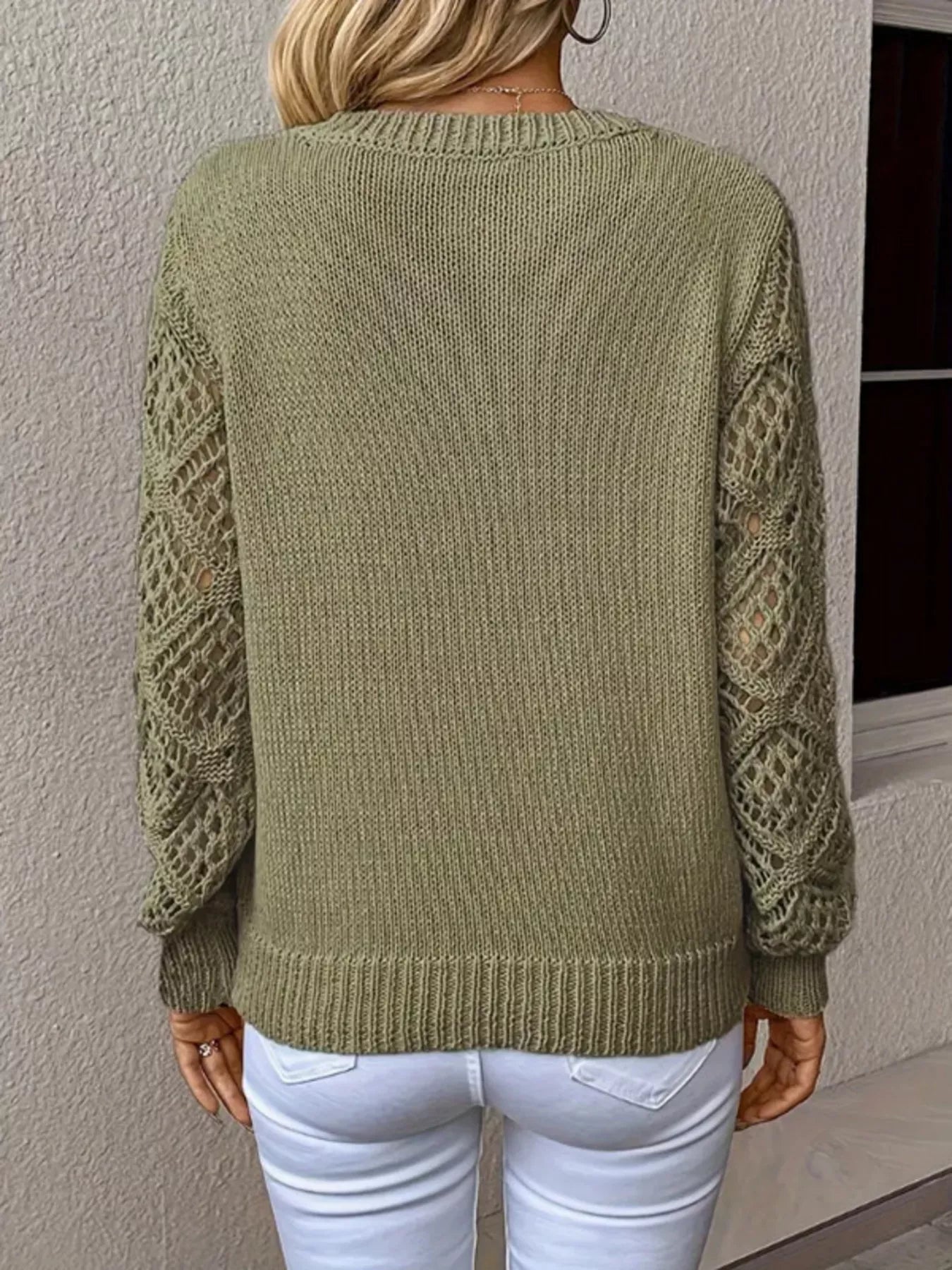 Person wearing a green knitted sweater with a textured pattern, standing against a neutral wall.