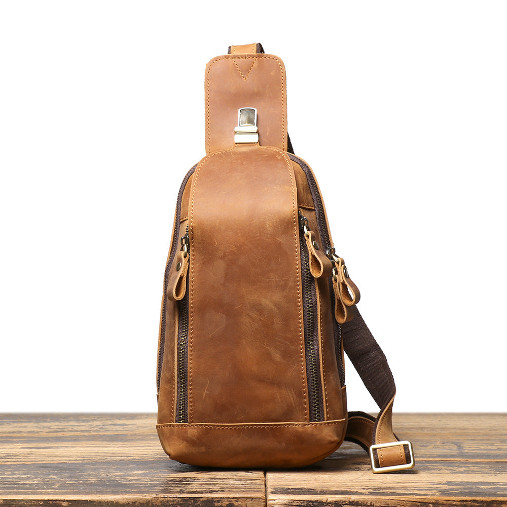 Brown leather sling bag on a wooden surface with a white background