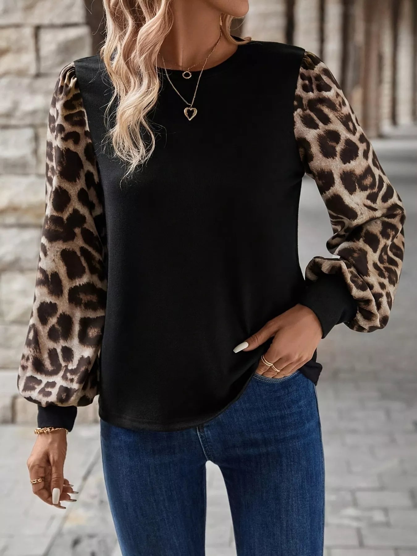Person wearing a black top with leopard print sleeves and blue jeans.